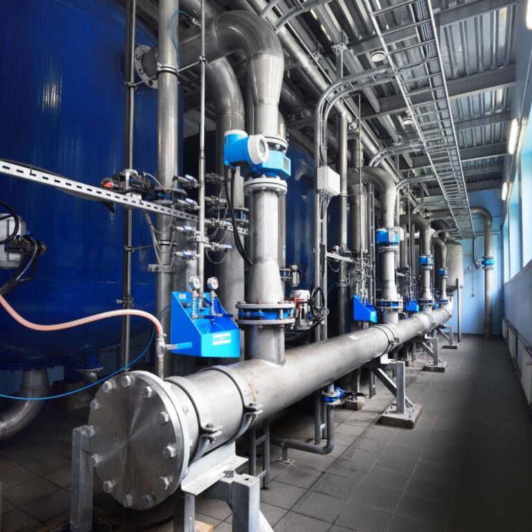 Industrial piping system with blue tanks and valves, showcasing a modern water treatment facility. The image highlights stainless steel pipes, pressure gauges, and control panels, emphasizing efficiency in fluid management and infrastructure design.